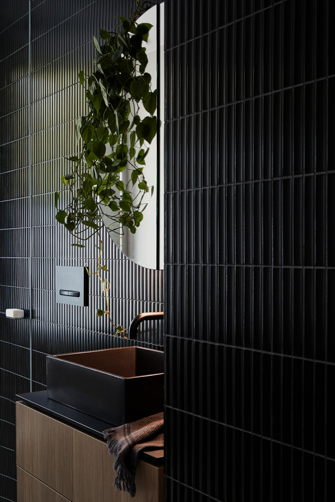 Photo of a mid-sized industrial 3/4 bathroom in Melbourne with flat-panel cabinets, medium wood cabinets, black tile, a vessel sink, grey floor, black benchtops, a single vanity and a floating vanity.