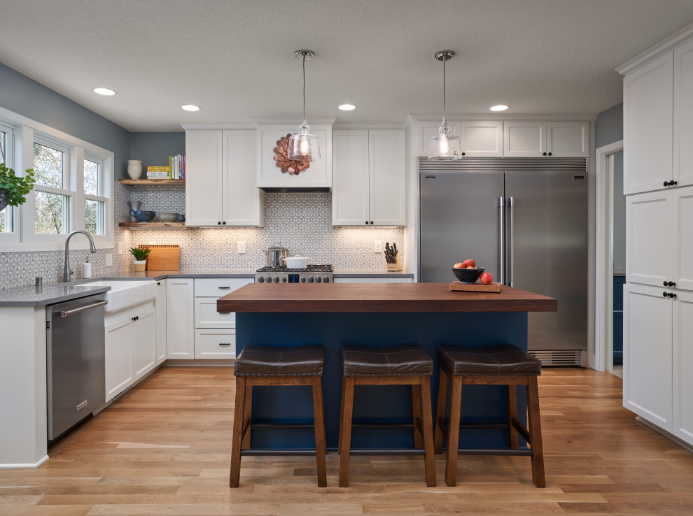Inspiration for a transitional u-shaped medium tone wood floor and brown floor kitchen remodel in Minneapolis with a farmhouse sink, shaker cabinets, white cabinets, wood countertops, gray backsplash, stainless steel appliances, an island and brown countertops