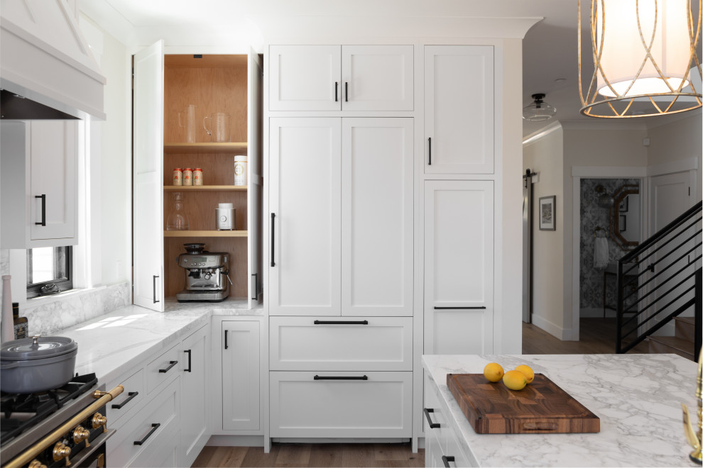 Design ideas for a mid-sized beach style l-shaped eat-in kitchen in Other with a farmhouse sink, recessed-panel cabinets, white cabinets, marble benchtops, white splashback, marble splashback, panelled appliances, medium hardwood floors, with island, beige floor and white benchtop.
