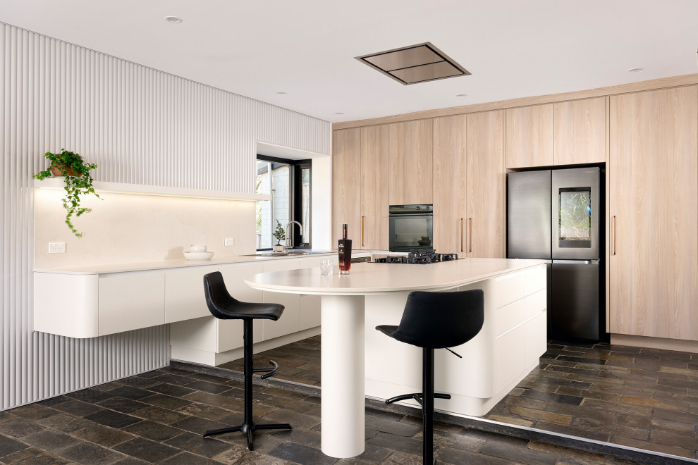This is an example of a large scandi l-shaped kitchen/diner in Perth with a double-bowl sink, flat-panel cabinets, white cabinets, engineered stone countertops, white splashback, engineered quartz splashback, black appliances, slate flooring, an island, black floors and white worktops.