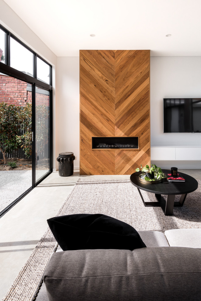 Источник вдохновения для домашнего уюта: маленькая открытая гостиная комната в стиле модернизм с бетонным полом, стандартным камином, фасадом камина из дерева, телевизором на стене и серым полом для на участке и в саду