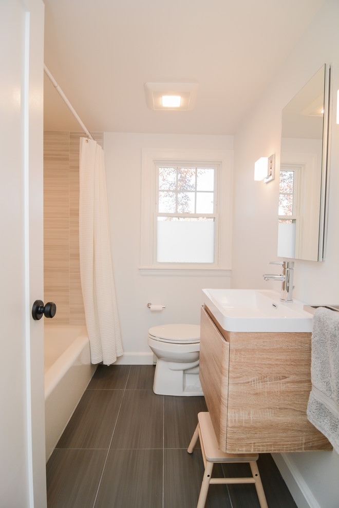 Photo of a mid-sized modern bathroom in Boston with flat-panel cabinets, an alcove tub, a shower/bathtub combo, a two-piece toilet, beige tile, white walls, porcelain floors, an integrated sink, a shower curtain, white benchtops, beige cabinets, porcelain tile, engineered quartz benchtops and brown floor.