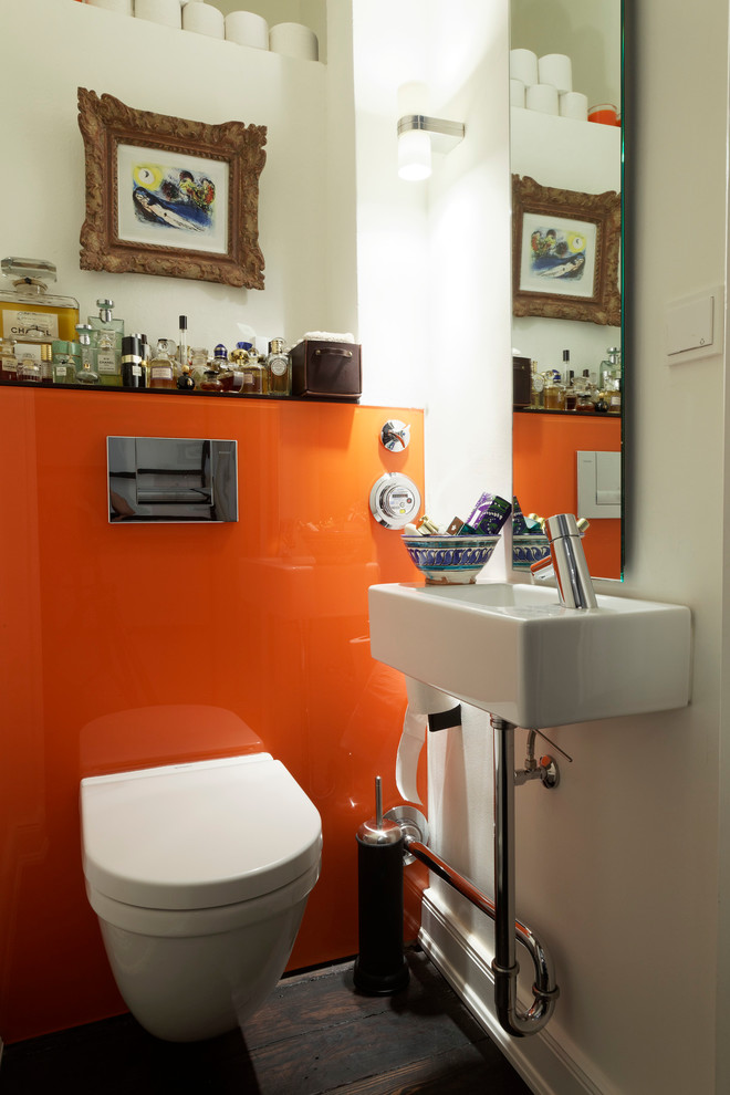 Design ideas for a small contemporary powder room in Hamburg with flat-panel cabinets, white cabinets, a two-piece toilet, glass sheet wall, orange walls, dark hardwood floors, a console sink, glass benchtops and brown floor.