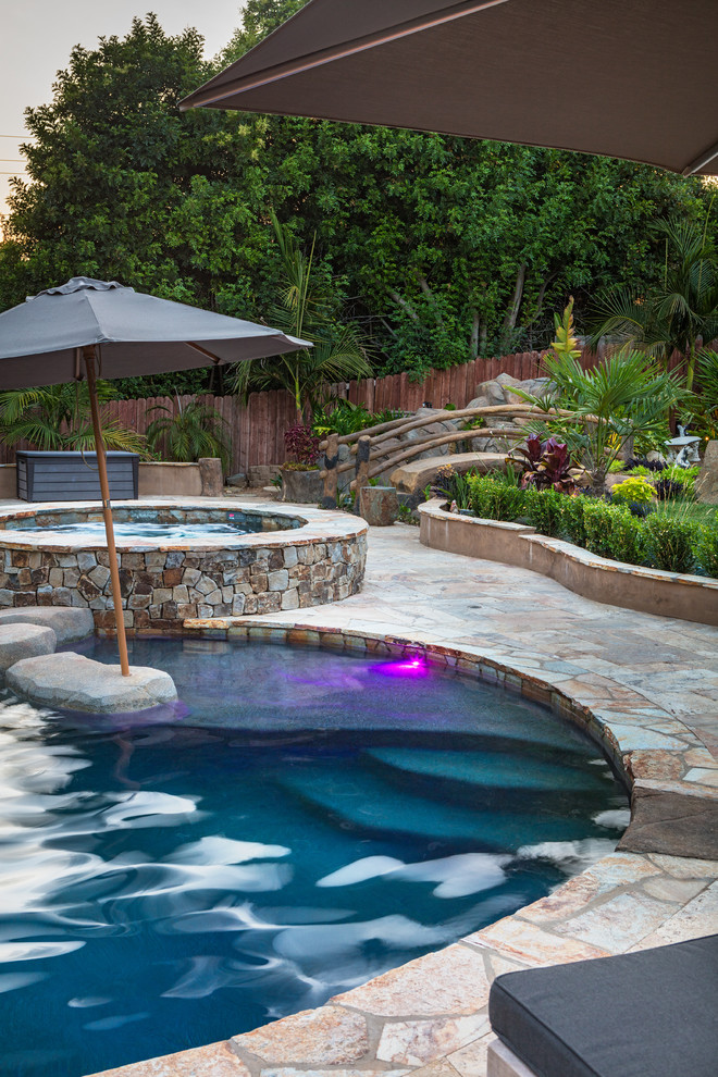 Inspiration for a large tropical backyard custom-shaped natural pool in San Diego with natural stone pavers.