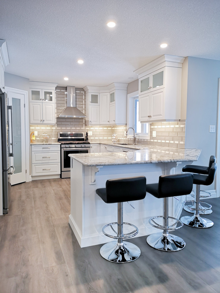 Inspiration for a mid-sized transitional u-shaped light wood floor and brown floor enclosed kitchen remodel in Toronto with an undermount sink, raised-panel cabinets, white cabinets, granite countertops, beige backsplash, glass tile backsplash, stainless steel appliances, a peninsula and gray countertops