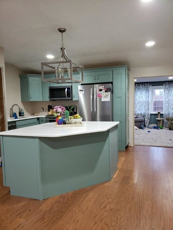 Inspiration for a large eclectic l-shaped eat-in kitchen in New York with an undermount sink, recessed-panel cabinets, blue cabinets, solid surface benchtops, stainless steel appliances, light hardwood floors, with island, yellow floor and white benchtop.