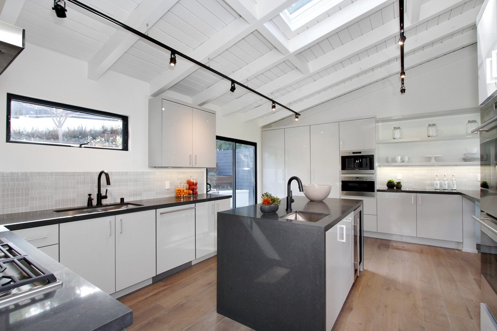 Photo of a mid-sized modern l-shaped eat-in kitchen in Los Angeles with flat-panel cabinets, grey cabinets, quartz benchtops, dark hardwood floors, multiple islands, an undermount sink, grey splashback, ceramic splashback and stainless steel appliances.