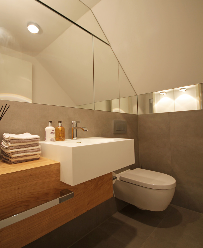 Gästetoilette With flächenbündigen Schrankfronten, hellen Holzschränken, Wandtoilette mit Spülkasten, grauen Fliesen, Steinfliesen, weißer Wandfarbe, Aufsatzwaschbecken, Mineralwerkstoff-Waschtisch, grauem Boden and Zementfliesen für Boden in Munich