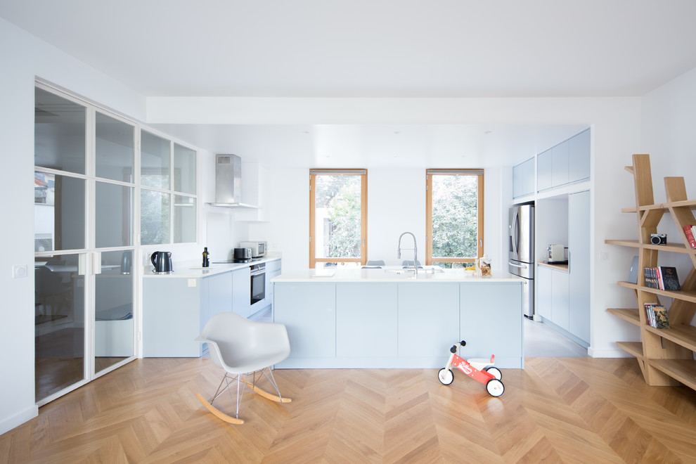 Large contemporary u-shaped open plan kitchen in Paris with an undermount sink, flat-panel cabinets, blue cabinets, white splashback, stainless steel appliances, light hardwood floors, with island, white benchtop, laminate benchtops and grey floor.