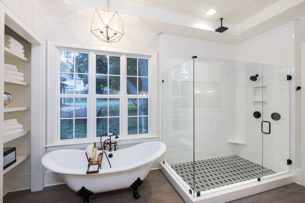 Photo of a large country master bathroom in Charlotte with a claw-foot tub, white tile, glass tile, beige walls, medium hardwood floors and a hinged shower door.