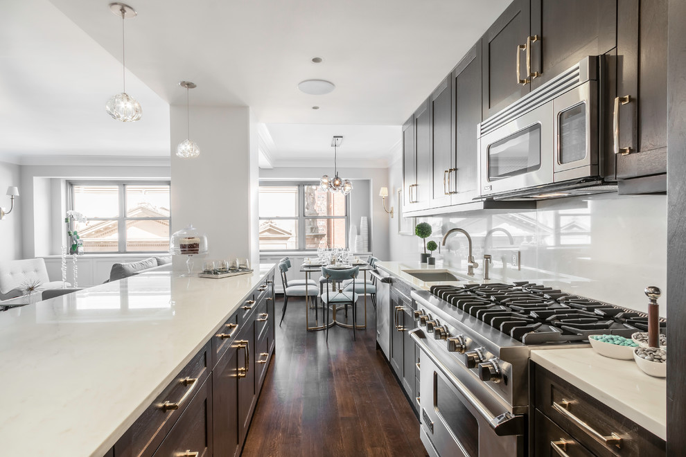 Transitional galley open plan kitchen in New York with an undermount sink, shaker cabinets, dark wood cabinets, white splashback, stainless steel appliances, dark hardwood floors and a peninsula.