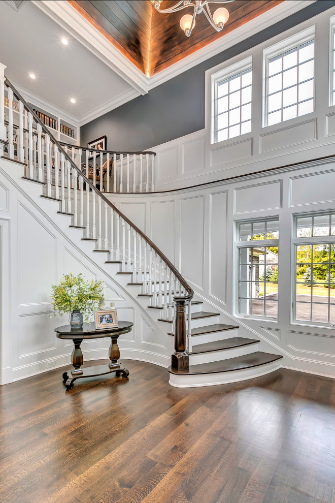 Photo of a large transitional wood curved staircase in New York with painted wood risers, wood railing and panelled walls.
