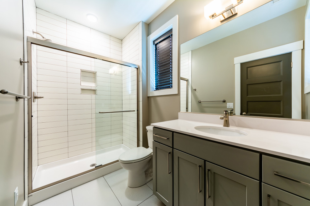 Photo of a mid-sized beach style 3/4 bathroom in Other with shaker cabinets, grey cabinets, an alcove shower, a two-piece toilet, grey walls, porcelain floors, an undermount sink, engineered quartz benchtops, white floor, a sliding shower screen and white benchtops.