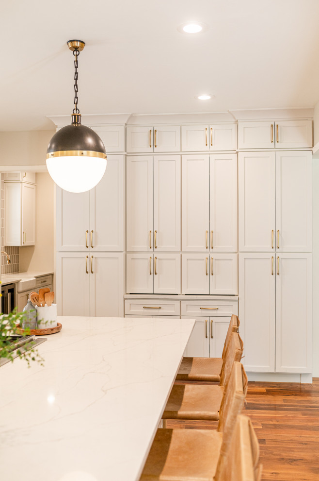 Example of a large transitional l-shaped dark wood floor and brown floor open concept kitchen design in Denver with a farmhouse sink, shaker cabinets, beige cabinets, quartz countertops, beige backsplash, ceramic backsplash, stainless steel appliances, an island and white countertops