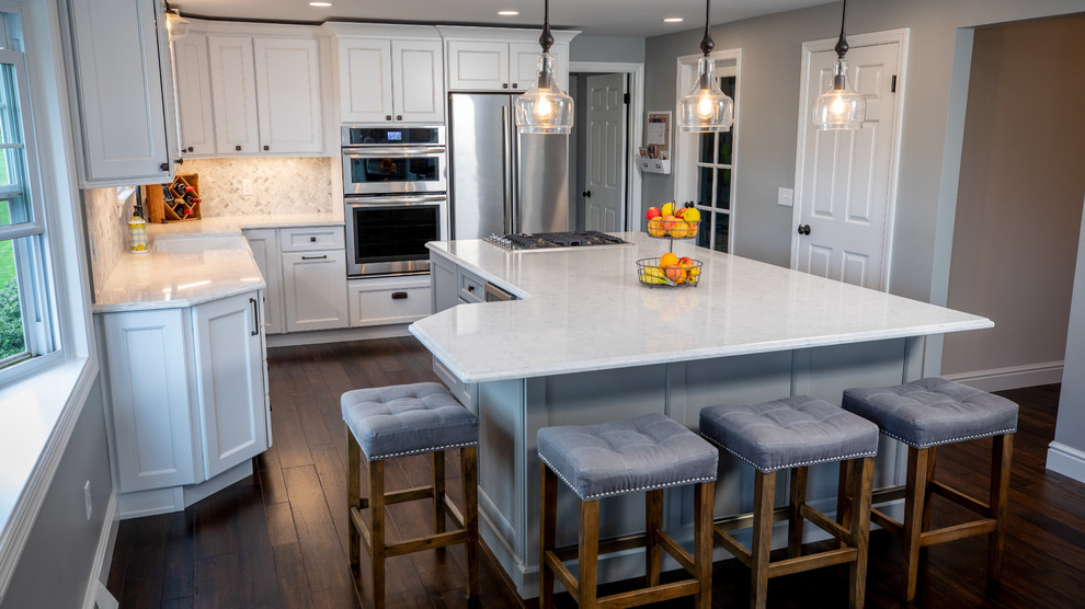 Large transitional u-shaped dark wood floor and brown floor eat-in kitchen photo with a farmhouse sink, recessed-panel cabinets, white cabinets, quartz countertops, white backsplash, marble backsplash, stainless steel appliances, an island and white countertops