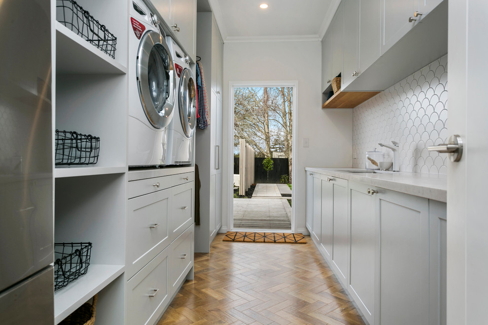 Mid-sized traditional galley utility room in Hamilton with a single-bowl sink, beaded inset cabinets, grey cabinets, marble benchtops, beige walls, laminate floors, a side-by-side washer and dryer and brown floor.
