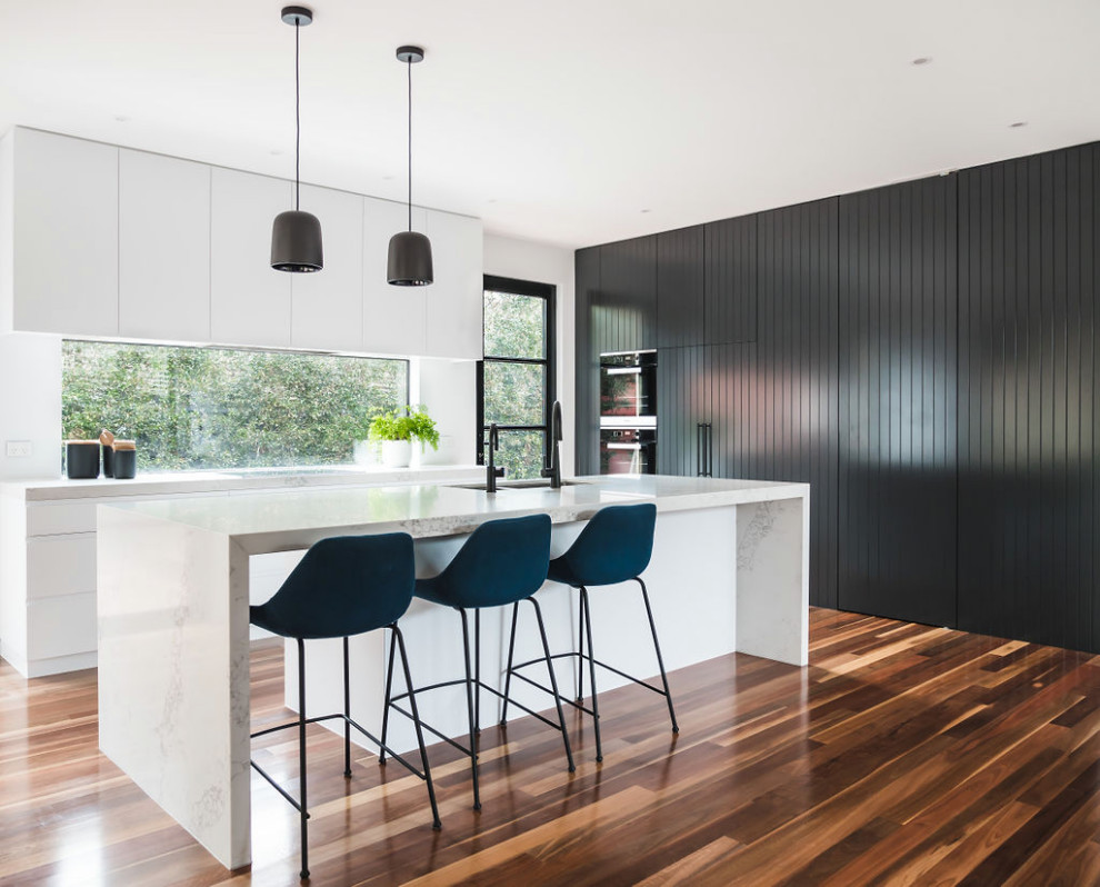 Photo of a contemporary l-shaped kitchen in Melbourne with an undermount sink, flat-panel cabinets, white cabinets, stainless steel appliances, dark hardwood floors, with island, brown floor and white benchtop.