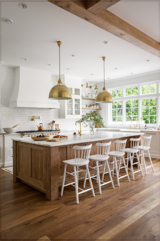 This is an example of a large transitional u-shaped open plan kitchen in Other with a farmhouse sink, shaker cabinets, white cabinets, marble benchtops, white splashback, subway tile splashback, panelled appliances, medium hardwood floors, with island, brown floor, white benchtop and exposed beam.