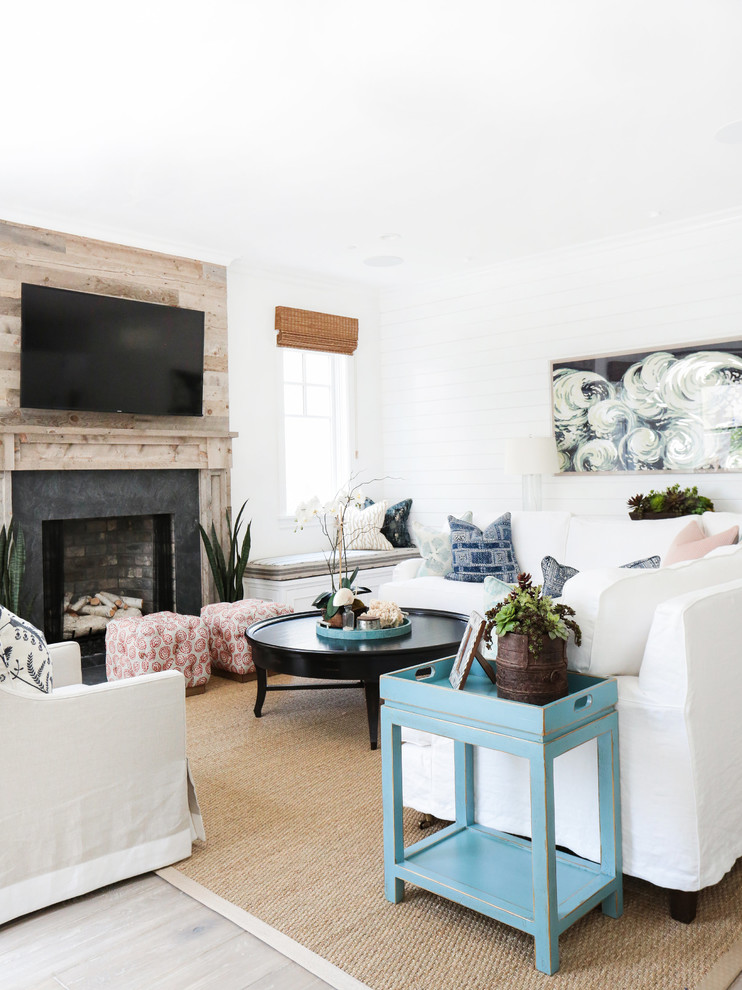 Photo of a mid-sized beach style enclosed living room in Orange County with white walls, light hardwood floors, a standard fireplace, a wood fireplace surround and a wall-mounted tv.
