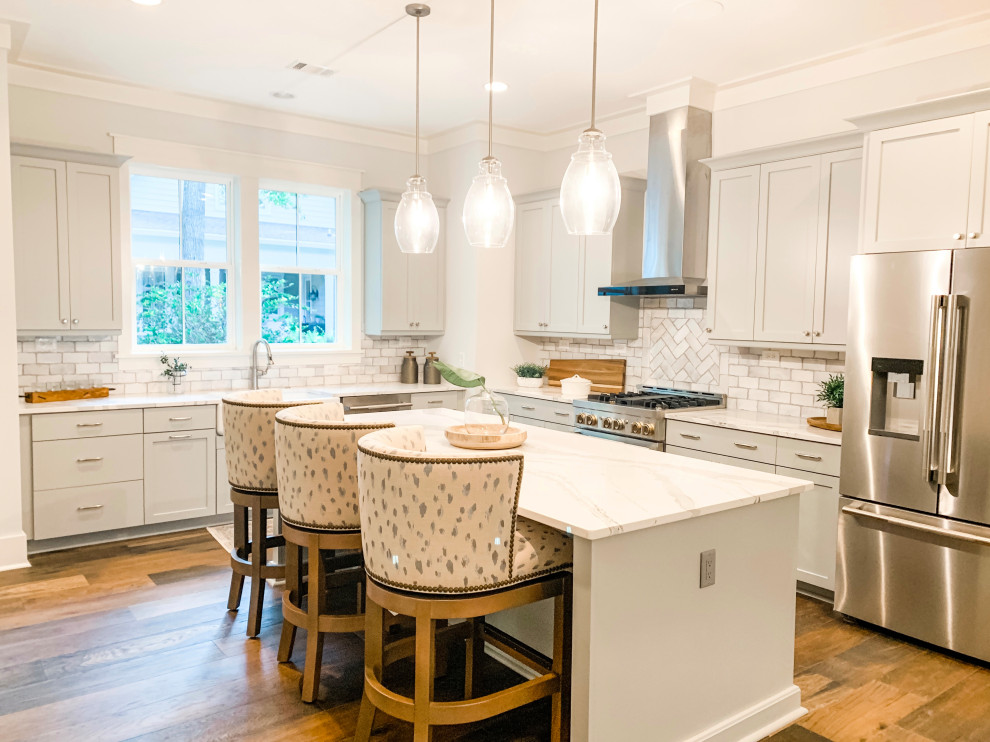 Mid-sized transitional l-shaped brown floor eat-in kitchen photo with a farmhouse sink, shaker cabinets, gray cabinets, quartz countertops, gray backsplash, ceramic backsplash, stainless steel appliances, an island and white countertops