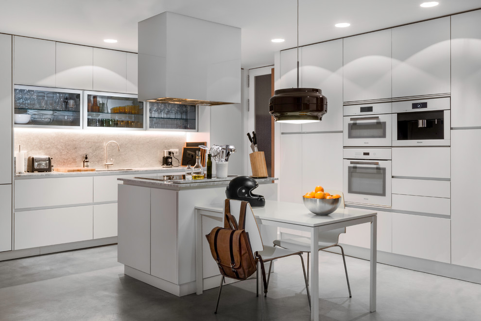 Inspiration for a large midcentury l-shaped separate kitchen in Madrid with an undermount sink, flat-panel cabinets, white cabinets, marble benchtops, white splashback, marble splashback, panelled appliances, concrete floors, with island and grey floor.