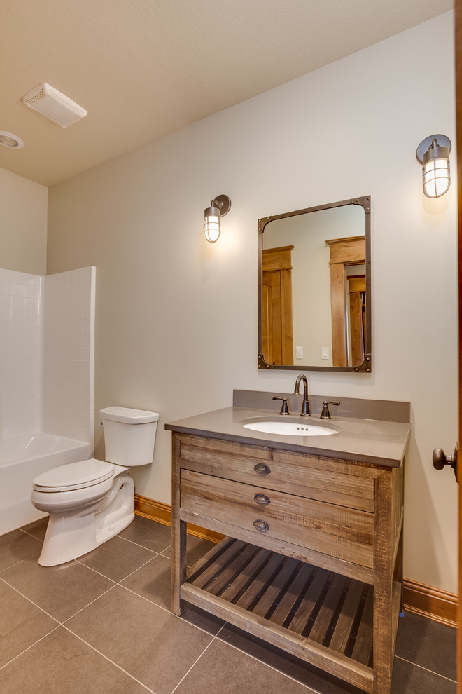 Photo of a mid-sized country kids bathroom in Other with an undermount sink, furniture-like cabinets, quartzite benchtops, an alcove tub, an open shower, a two-piece toilet, gray tile, ceramic tile, beige walls, ceramic floors and medium wood cabinets.