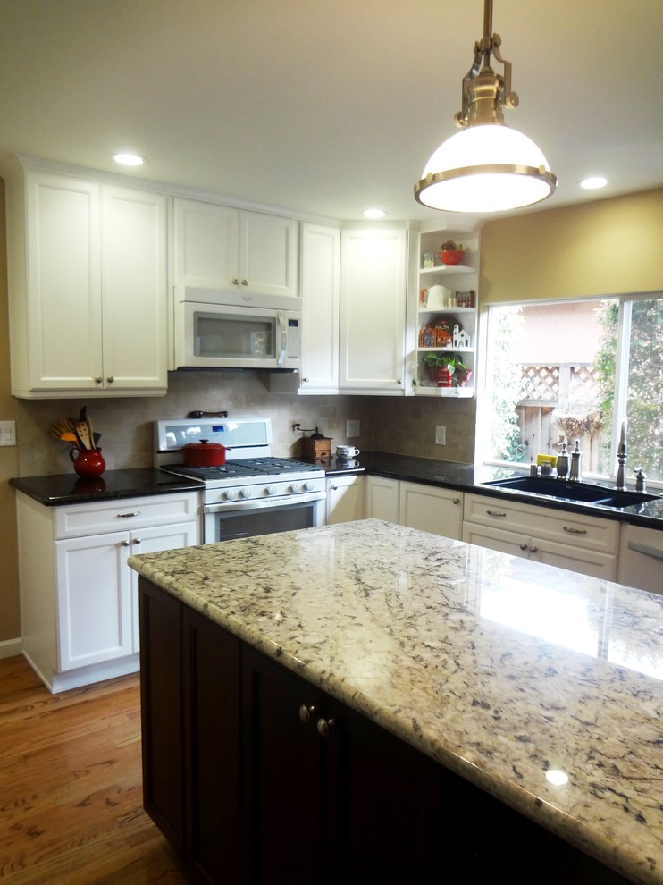 Mid-sized transitional l-shaped kitchen pantry in San Francisco with an undermount sink, recessed-panel cabinets, white cabinets, granite benchtops, beige splashback, porcelain splashback, white appliances, medium hardwood floors and with island.