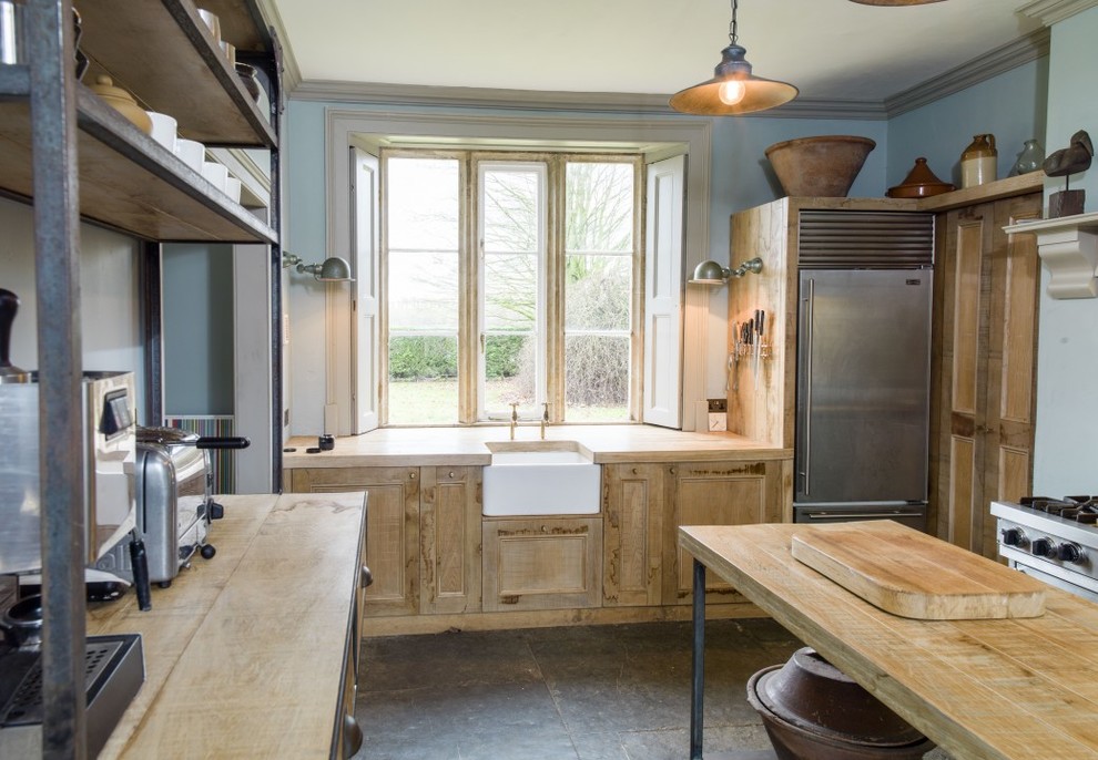 Large country u-shaped eat-in kitchen in Wiltshire with a farmhouse sink, wood benchtops, with island, distressed cabinets, stainless steel appliances, slate floors and shaker cabinets.