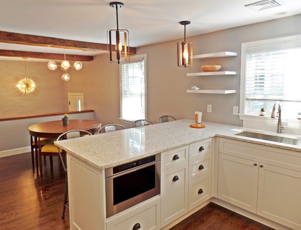 This is an example of a mid-sized transitional u-shaped eat-in kitchen in Other with an undermount sink, shaker cabinets, white cabinets, quartz benchtops, white splashback, subway tile splashback, stainless steel appliances, medium hardwood floors, a peninsula, brown floor and white benchtop.