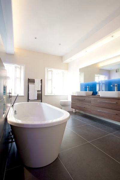 Inspiration for an expansive contemporary master bathroom in Oxfordshire with a vessel sink, flat-panel cabinets, medium wood cabinets, glass benchtops, a freestanding tub, a double shower, a two-piece toilet, brown tile, porcelain tile, blue walls and porcelain floors.