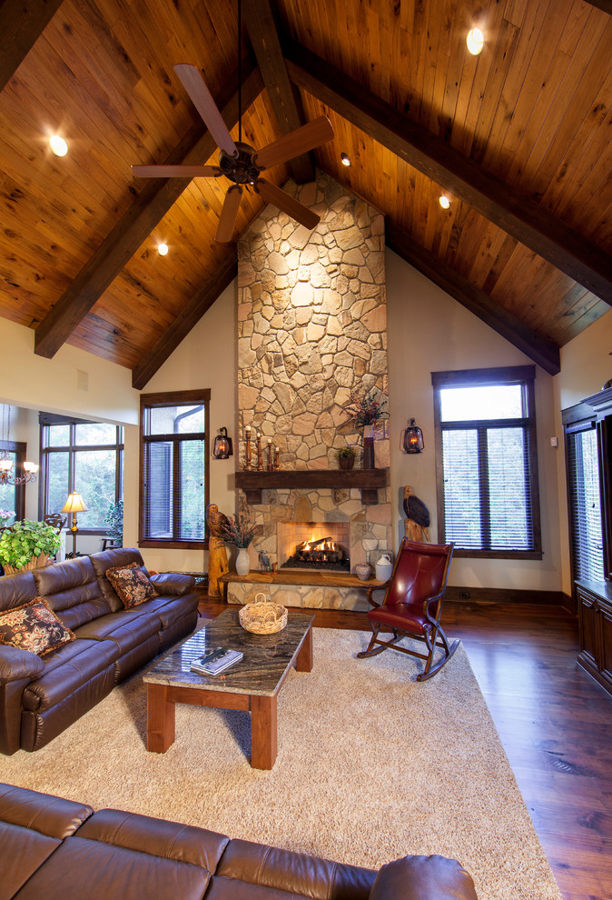 This is an example of a large country open concept family room in Charlotte with beige walls, dark hardwood floors, a standard fireplace, a stone fireplace surround, a freestanding tv and brown floor.