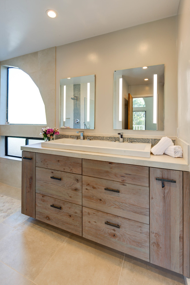 Photo of a mid-sized beach style master bathroom in San Francisco with flat-panel cabinets, distressed cabinets, a curbless shower, a one-piece toilet, beige tile, porcelain tile, beige walls, porcelain floors, a trough sink and tile benchtops.