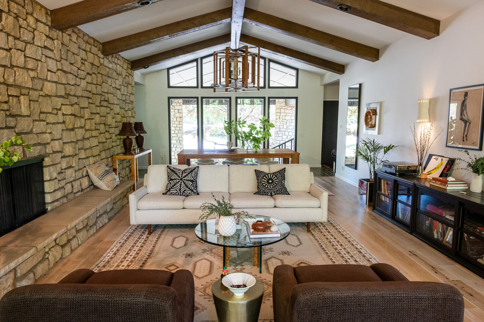 This is an example of a large transitional living room in Other with white walls, light hardwood floors, a two-sided fireplace, a stone fireplace surround, beige floor and vaulted.