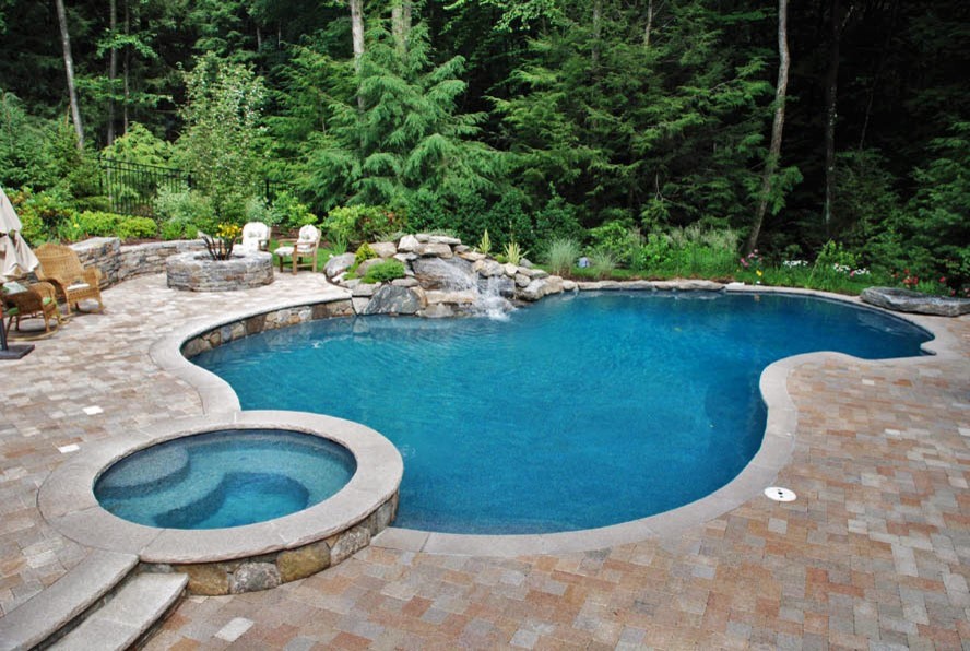Photo of a large modern backyard custom-shaped pool in New York with a hot tub and stamped concrete.