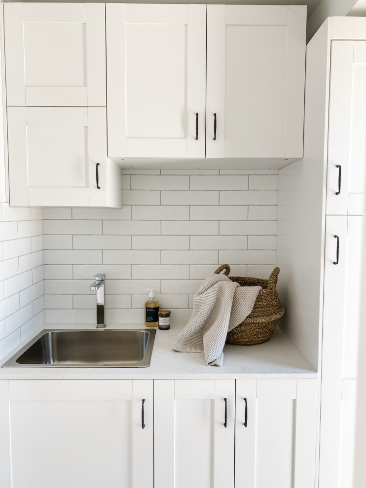 Exempel på en liten tvättstuga enbart för tvätt, med skåp i shakerstil, vita skåp, bänkskiva i kvarts, vitt stänkskydd, stänkskydd i tunnelbanekakel, vita väggar och ljust trägolv