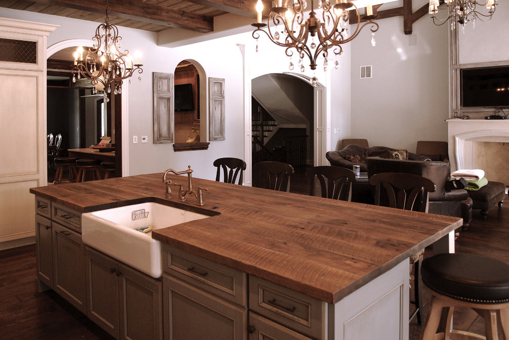 This is an example of a country l-shaped eat-in kitchen in Chicago with recessed-panel cabinets, white cabinets, wood benchtops, dark hardwood floors, with island, brown floor, brown benchtop, exposed beam and a farmhouse sink.