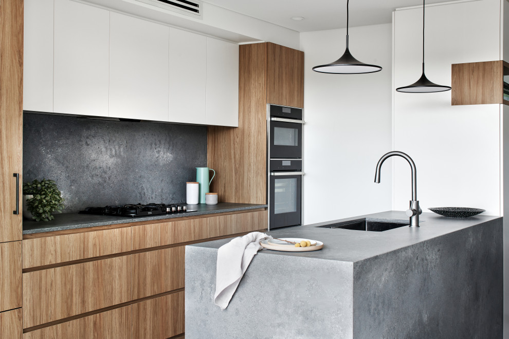 This is an example of a mid-sized modern galley eat-in kitchen in Sydney with an undermount sink, flat-panel cabinets, medium wood cabinets, glass benchtops, grey splashback, stone slab splashback, black appliances, a peninsula and grey benchtop.