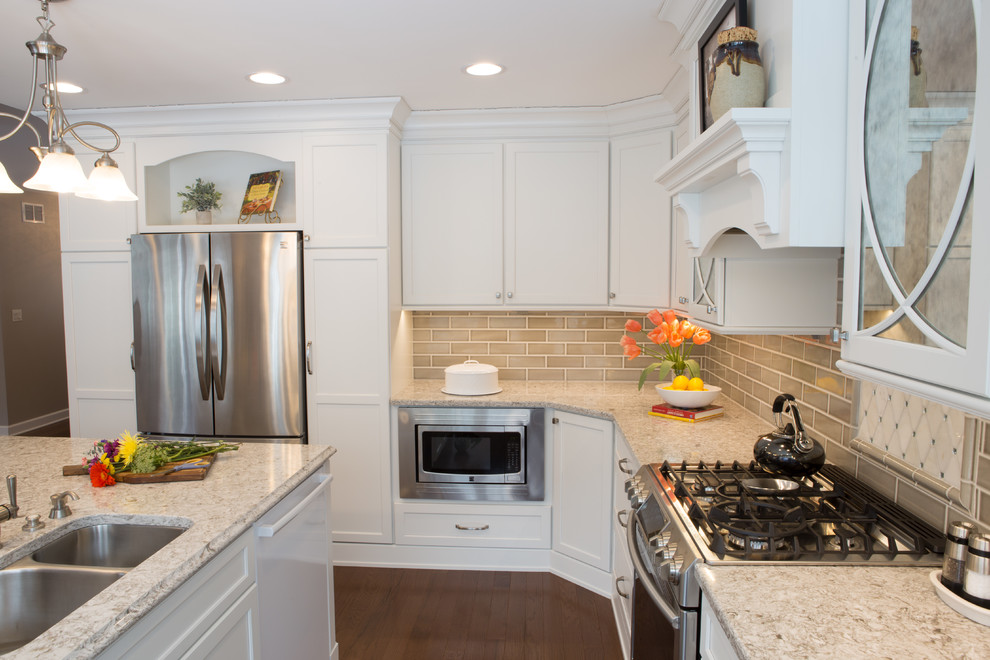 Example of a large classic u-shaped light wood floor and brown floor kitchen design in Chicago with an undermount sink, recessed-panel cabinets, white cabinets, quartz countertops, beige backsplash, ceramic backsplash, stainless steel appliances and an island