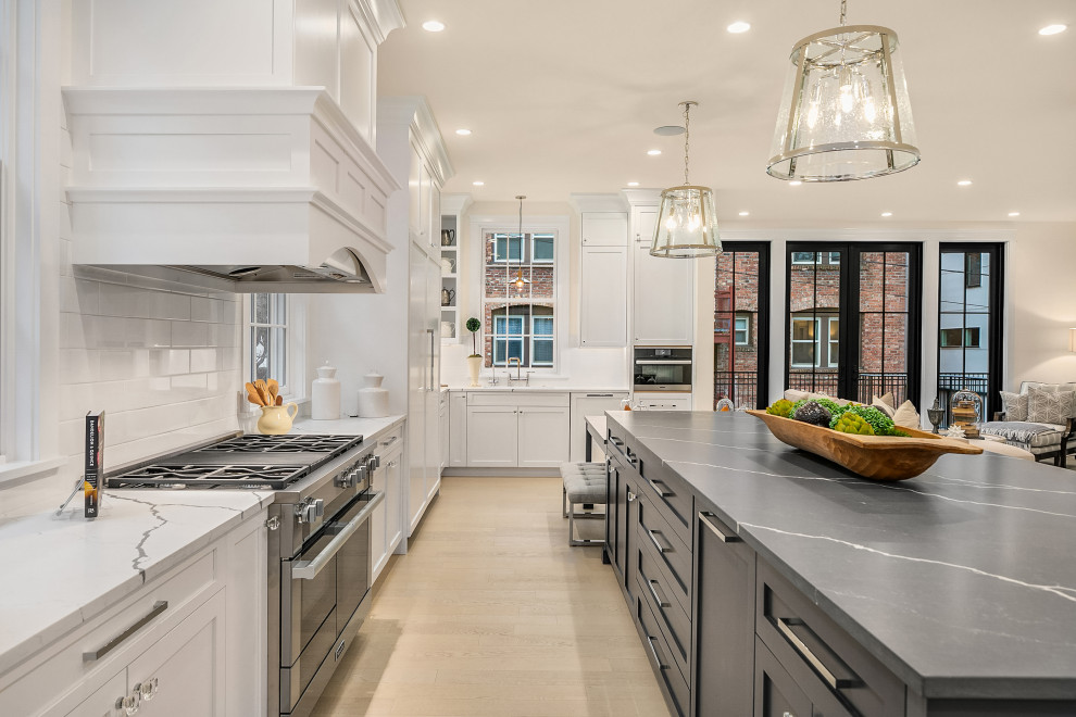 Transitional l-shaped kitchen in Seattle with shaker cabinets, white cabinets, white splashback, stainless steel appliances, light hardwood floors, with island, beige floor and white benchtop.