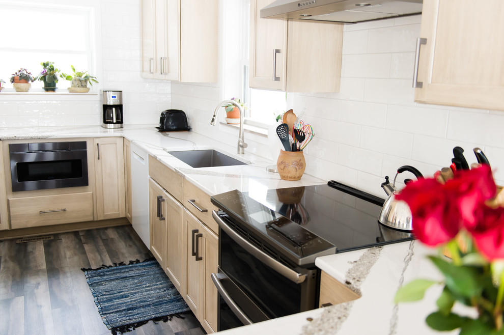 Mid-sized transitional u-shaped vinyl floor and brown floor enclosed kitchen photo with an undermount sink, flat-panel cabinets, beige cabinets, quartz countertops, white backsplash, subway tile backsplash, black appliances, a peninsula and white countertops