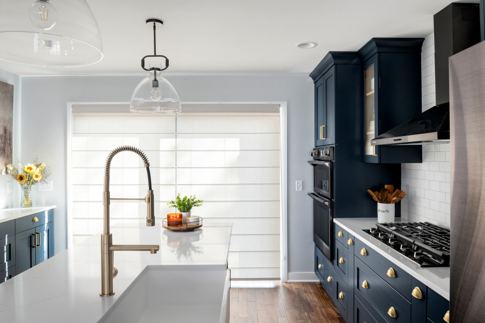 This is an example of a mid-sized transitional single-wall eat-in kitchen in Minneapolis with a single-bowl sink, flat-panel cabinets, blue cabinets, quartz benchtops, white splashback, ceramic splashback, black appliances, dark hardwood floors, with island, brown floor and white benchtop.