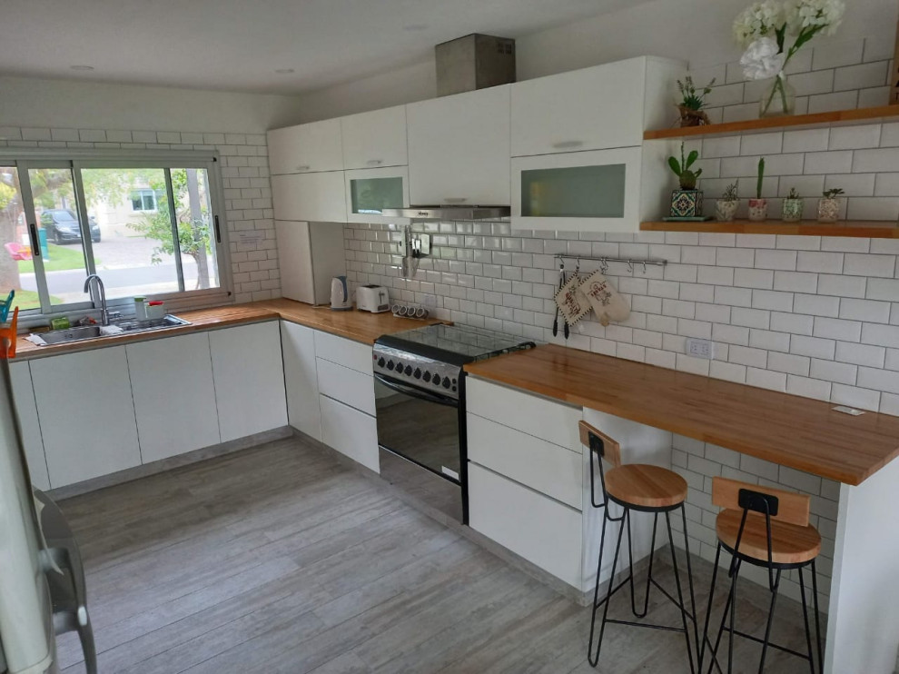 This is an example of a large contemporary u-shaped eat-in kitchen in Other with a double-bowl sink, flat-panel cabinets, white cabinets, wood benchtops, white splashback, ceramic splashback, stainless steel appliances, porcelain floors, no island, grey floor, beige benchtop and recessed.