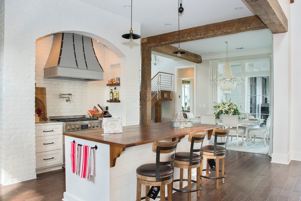Photo of a traditional eat-in kitchen in New Orleans with shaker cabinets, white cabinets, wood benchtops, white splashback, subway tile splashback, stainless steel appliances, dark hardwood floors and with island.