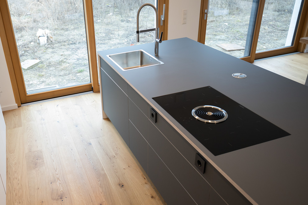 Photo of a large modern single-wall open plan kitchen in Stuttgart with flat-panel cabinets, white cabinets, laminate benchtops, with island, blue benchtop, an integrated sink, medium hardwood floors and brown floor.