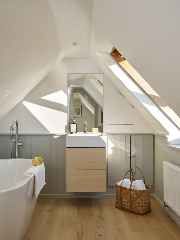 This is an example of a mid-sized scandinavian kids bathroom in Hampshire with flat-panel cabinets, light wood cabinets, a freestanding tub, grey walls, light hardwood floors, brown floor and a console sink.