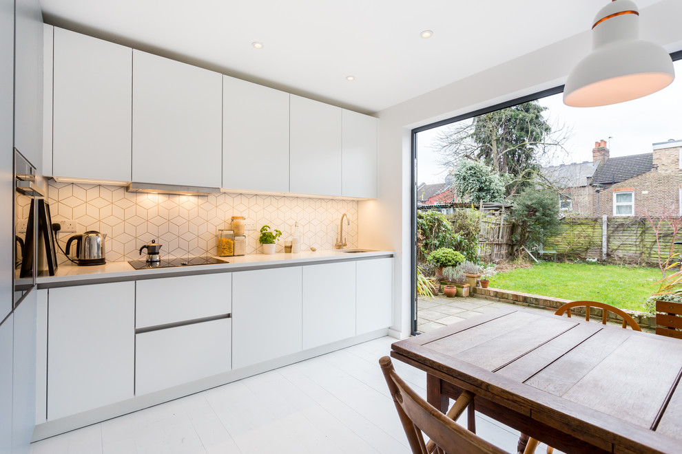 This is an example of a mid-sized modern single-wall eat-in kitchen in London with flat-panel cabinets, white cabinets, quartzite benchtops, no island, white splashback, black appliances, painted wood floors and white floor.