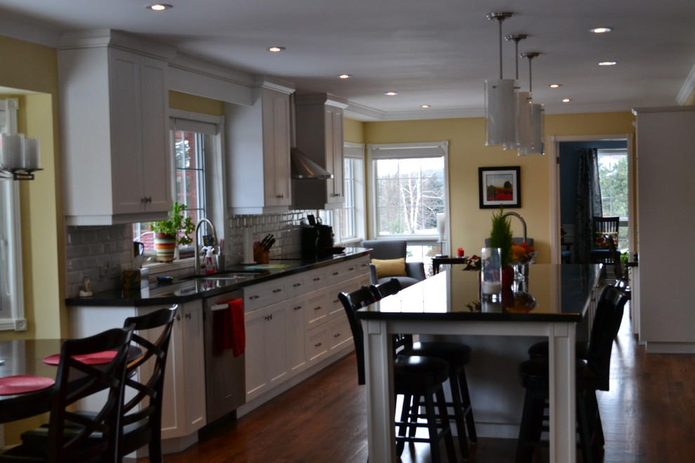 Large transitional galley medium tone wood floor eat-in kitchen photo in Toronto with a double-bowl sink, shaker cabinets, white cabinets, granite countertops, white backsplash, subway tile backsplash, stainless steel appliances and an island