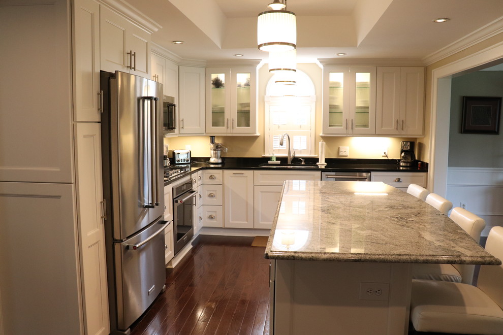 Eat-in kitchen - large transitional l-shaped medium tone wood floor and brown floor eat-in kitchen idea in New York with a double-bowl sink, shaker cabinets, white cabinets, quartzite countertops, beige backsplash, stainless steel appliances, an island and black countertops