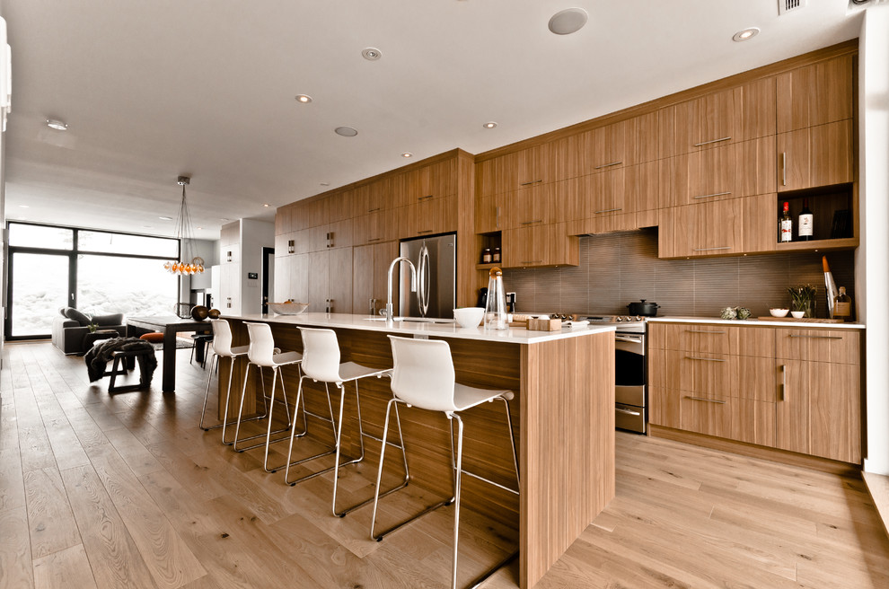 На фото: параллельная кухня-гостиная в современном стиле с плоскими фасадами, фасадами цвета дерева среднего тона, коричневым фартуком и техникой из нержавеющей стали с