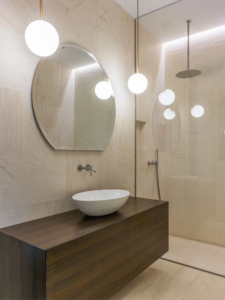 This is an example of a modern bathroom in Milan with flat-panel cabinets, dark wood cabinets, a curbless shower, beige tile, beige walls, a vessel sink, wood benchtops, beige floor, an open shower and beige benchtops.
